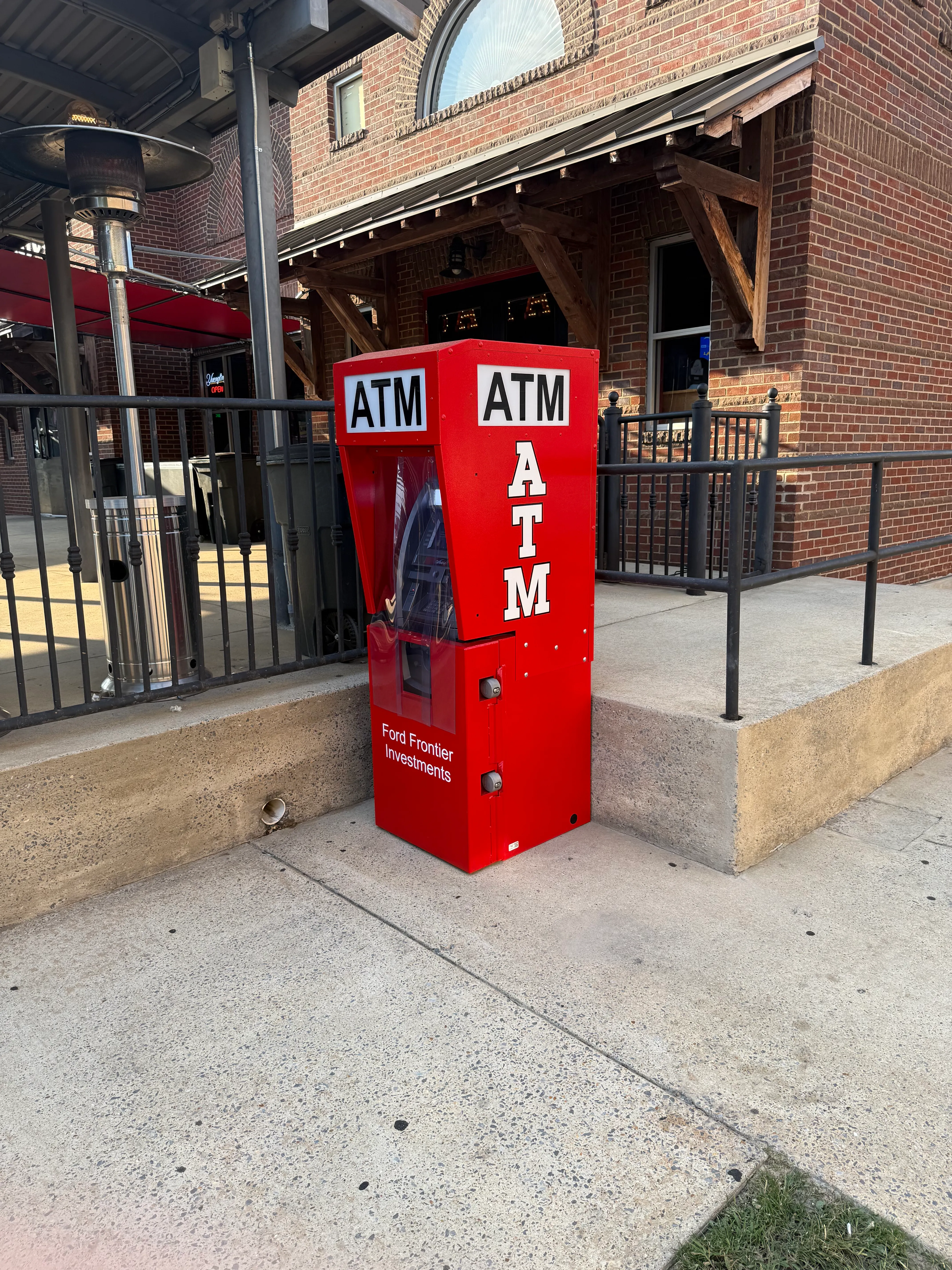 Ford Frontier Investments outdoor ATM installation — Genmega machine in branded red kiosk on Tuscaloosa sidewalk